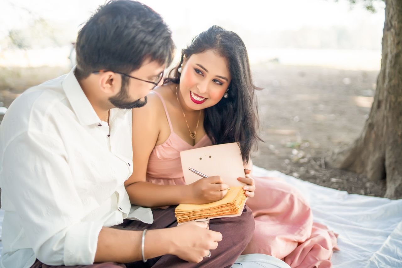 Hello world! A couple enjoying a romantic picnic outdoors, writing on a notebook.