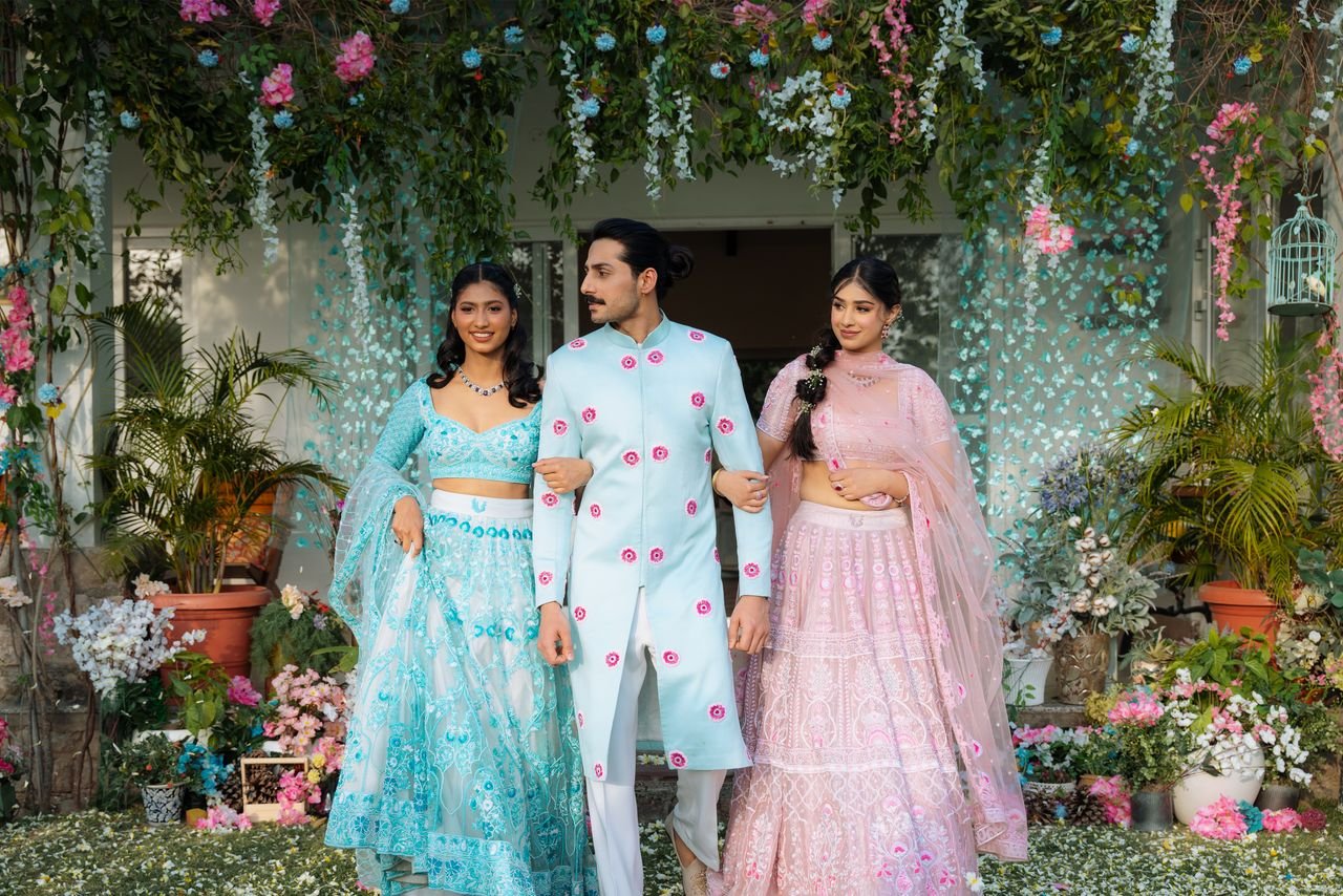 Three young adults in elegant attire at an outdoor wedding with vibrant floral decorations.